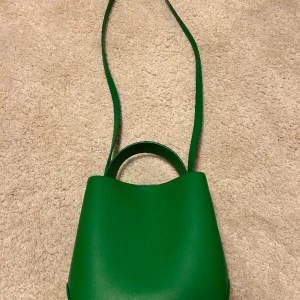 Väska från Gina Tricot - Ärtgrön handväska från Gina Tricot.  Använd en gång på ett tema-bröllop och nu hänger den bara i garderoben.  Mått utan remmar. 20x20x12