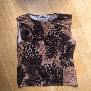 Mönstrad ärmlös topp från Pimkie - En ärmlös topp med ett unikt mönster som kombinerar leopard och blommor i olika nyanser av brunt och beige. Toppen har en rund halsringning och är tillverkad i ett mjukt material.