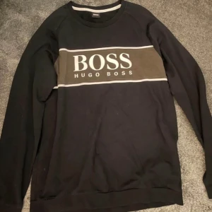 Svart tröja från Hugo Boss - En svart långärmad tröja från Hugo Boss. Tröjan har en rund halsringning och ribbstickade muddar vid ärmslut och nederkant.