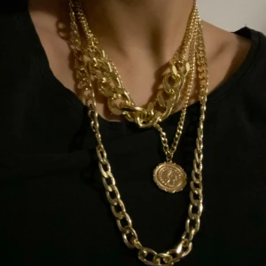 Guldhalsband med medaljong - Ett guldhalsband med flera kedjor och en medaljong. Halsbandet har en tjock kedja och en tunnare kedja med en rund medaljong som hänge.