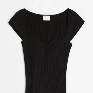 Svart ribbad topp - En svart ribbad topp med korta ärmar och en fyrkantig halsringning. Toppen har en tight passform och är tillverkad i ett stretchigt material.