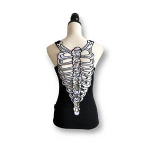 Svart linne med skelettmönster - Ett svart linne med ett unikt skelettmönster på ryggen. Linnet har breda axelband och en rund halsringning. Perfekt för en edgy och unik stil. Superfint skick!