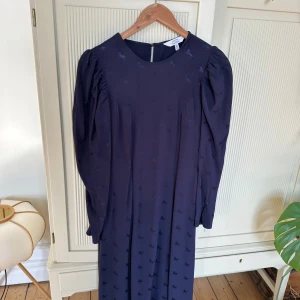 Mörkblå midiklänning, & other stories - Knappt använd klänning. Som ny. Klockad kjol och slits. Figursydd. Puffärm. Mönstrat tyg: små diskreta hästar i samma färg som botten. Material: Viscose