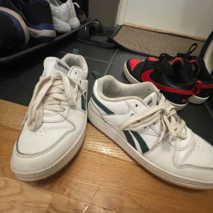 Vita Reebok sneakers - Ett par vita Reebok sneakers med gröna detaljer och snörning. Skorna har en klassisk design med Reebok-logotypen på sidan och tungan.