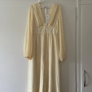 Blommig klänning  - Blommig gul långärmad klänning ifrån NA-KD i storlek M.Klänningen är helt oanvänd,i väldigt fint skick och har prislapp kvar.Klänningen har  knappar framtill med en liten slits fram och ger fin form i midjan.Nypris 999 säljs 500 pris kan diskuteras