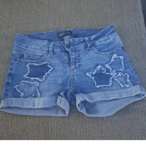 Ett par blå jeansshorts från Only med stjärnformade slitningar på framsidan. Shortsen har upprullade benslut och klassisk femficksdesign.