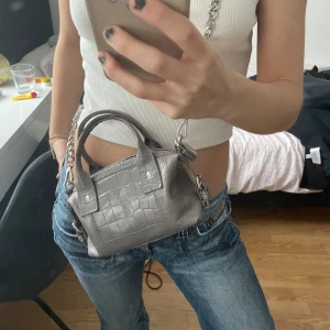Nunoo väska - Säljer min ”Mini bobby croco dark grey” väska som inte längre går att köpa! Orginalpris: 1020kr på núnoos hemsida 💘 Färgen är grå/lila