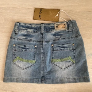 Lågmidjad jeanskjol - Jeanskjol med låg midja. Sista bilden visar färgen bäst. Midjemåttet är 37, längden är 31 cm💗Snygga fickor med sömmar och detaljer på märket. Lappen finns kvar, visar storlek XL. Men det är barnstorlek så skulle snarare uppskatta storlek S❤️