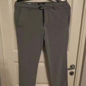 Kostymbyxor - Gråa kostymbyxor från Jack & Jones. Två fickor framtill samt två fickor baktill, försluts med dragkedja och knapp.