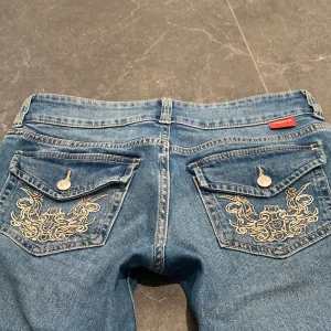 Lågmidjade jeans - Säljer dessa skit snygga jeans för att jag it använder dem längre. Den är lågmidjade och har 2 knappar där fram och dem är Bootcut. Dem har fickor med skit snygga tryck💞dem är i bra skick och har bara använt några gånger💖original pris 300kr