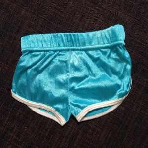 Grönblå shorts strl. 62 - Grönblå, petrolfärgade, shorts. Retro. Ungefär storlek 62, se jämförelse med ett par shorts från Adidas i storlek 62 på bild 3. I fint begagnat skick, inga hål eller fläckar.  Tvättade i parfymfritt tvättmedel och utan sköljmedel.