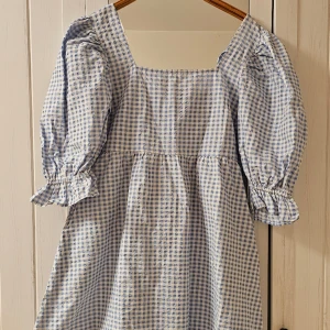 Holly whyte klänning  -  Klänning, holly whyte stl L. Underbart söt klänning i ljusblå-vita rutor med stor rosett i ryggen. Smock i ryggen, dragkedja i sidan. Dolda fickor. Puffärmar och volang längst ut på ärmen. I nyskick, endast använd en gång