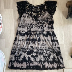 Blus/klänning -  jättesnygg blus liknande klänning med v ringning och svart spets på överdelen och grå svart mönster under.  Man kan knyta en rosett med snören på bakdelen som ger en söt ”touch”💗 Superfint skick!