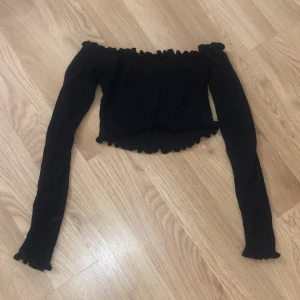 Långärmad tröja  - Den är svart och har volanger på sig.