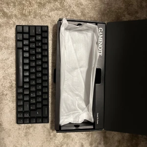 Gamenote KB61 Mechanical Keyboard - Kompakt mekaniskt tangentbord från Gamenote, modell KB61. Svart färg, 61 tangenter, perfekt för gaming och arbete. Levereras med originalkartong. Tangentbordet   Är i mycket gott skick utan  slitage eller defekter. Den har sladd i kartongen, den fungerar även utan sladd genom bluetooth. Den har även ljus i tangentbordet 