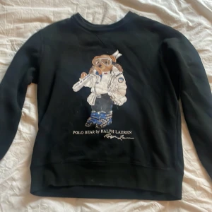 Svart sweatshirt Polo Ralph Lauren M - Svart sweatshirt från Polo Ralph Lauren med ikonisk Polo Bear-tryck på framsidan. Tröjan har rund hals, långa ärmar och ribbade muddar. Materialet är mjuk bomull och passformen är normal. Perfekt för dig som gillar streetstyle och klassiska märken. Pris kan diskuteras vid snabb affär!
