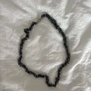 Svart halsband med oregelbundna stenar - Unikt svart halsband med oregelbundna, glansiga stenar som ger en cool och edgy vibe. Halsbandet har ett metallspänne och passar perfekt för dig som gillar att sticka ut med accessoarer. Snyggt att matcha med både streetwear och mer stilrena outfits.