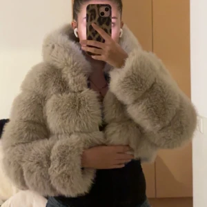 Beige fluffig pälsjacka med huva - Supermjuk och fluffig beige pälsjacka med stor huva och breda ärmar. Jackan är croppad och har ett lyxigt, oversized uttryck. Perfekt för dig som vill sticka ut och hålla dig varm med stil. Fodret har ett unikt mönster och jackan är riktigt cozy. Säljer då den är för liten på mig, för referens jag är 162 lång, och har vanligtvis storlek S, denna jacka är i storlek XS