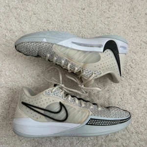 Nike sneakers Sabrina 1 beige och svart - Säljer ett par snygga Nike sneakers i beige och svart med coolt rutigt mönster på ovandelen. Skorna har tydlig svart swoosh, snörning och vit sula. Ovandelen är i mesh och syntet för en sportig vibe. Perfekta för dig som gillar stilrena men unika sneakers.