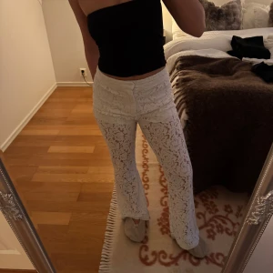 Vita spetsbyxor med utsvängda ben - Säljer ett par vita byxor i spets med utsvängda ben. Byxorna är högmidjade och har ett snyggt blommigt spetsmönster över hela tyget. Perfekta för dig som vill sticka ut och köra en trendig look. Dom är smutsiga nedtill! Men inget man tänker på när man har på sig dem