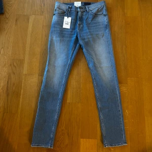Blå slim fit jeans Tiger of Sweden W29 L32 - Snygga blå jeans från Tiger of Sweden med klassisk femficksdesign och skinny passform. Jeansen har en ljus tvätt och raka ben, med normal midja och diskreta detaljer. Perfekta för dig som gillar stilrena och moderna jeans. Helt nya med prislapparna kvar