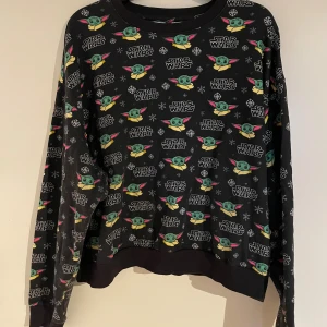 Star Wars tröja med Baby Yoda, XL - Svart långärmad tröja från H&M Divided i storlek XL med färgglatt Baby Yoda- och Star Wars-tryck över hela plagget. Tröjan har ribbad hals och muddar, samt snöflingor som extra detalj i mönstret. Perfekt för dig som älskar Star Wars och vill sticka ut.
