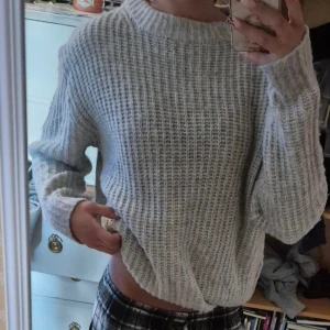 Ljusgrå stickad tröja från 157 - Mysig ljusgrå stickad tröja från 157 i storlek S. Tröjan har ett grovt ribbat mönster, rund hals och långa ärmar. Perfekt för att hålla sig varm under kyliga dagar och passar dig som gillar en enkel och chill stil. 