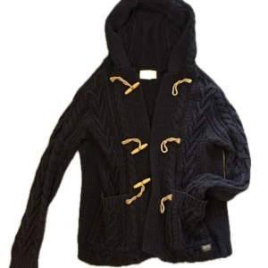 Mörkblå stickad kofta med huva Ralph Lauren - Mörkblå grovstickad kofta från Denim & Supply Ralph Lauren med huva och snygga snörningsdetaljer i beige. Koftan har två fickor framtill och coola träknappar. Storlek S men passar även M