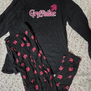 Harry Potter Gryffindor Pyjamasset - Ett set med en svart långärmad tröja och ett par matchande byxor. Tröjan har ett Gryffindor-tryck framtill med en tillhörande logotyp. Byxorna har ett mönster av Gryffindors vapensköld.