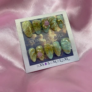 Dreamy(S):Short Almond;Curved  - Unika press-on naglar i mandelform med grönblå bas, guldiga detaljer, glitter och 3D-dekorationer som lila rosor och pärlor. Snyggt handmålat mönster och lyxig finish. Perfekt för dig som vill sticka ut med dina naglar.S: 15 mm, 11,5 mm, 12 mm, 11 mm, 9 mm 