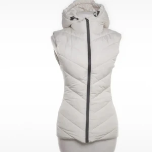Vit dunväst med huva och dragkedja - Snygg vit dunväst med huva och svart dragkedja framtill. Västen har ett quiltat mönster och justerbar snörning vid huvan. Perfekt för lager-på-lager och en clean look. Passformen är figurnära och västen är lätt att matcha med olika outfits.