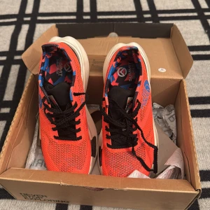 The North Face Summit Series sneakers - Säljer ett par snygga The North Face Summit Series sneakers i stark orange med svarta detaljer och blått mönstrat innerfoder. Skorna har mesh-ovandel, svart snörning och en kraftig vit plattformssula med svarta inslag. Perfekta för dig som gillar sportig stil och coola färger.