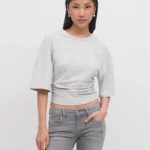 Grå topp med kort ärm - Säljer en ljusgrå topp med rund hals och korta ärmar. Toppen har en tight passform och är tillverkad i mjukt bomullsmaterial som sitter skönt mot kroppen. Perfekt för dig som gillar en enkel och clean stil med lite edge. Använd bara några få gånger