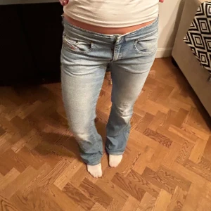Diesel ljusblå bootcut jeans - Säljer ett par ljusblå bootcut jeans från Diesel med klassisk logga på fickan. Jeansen har låg midja, raka ben med lätt utsvängning och snygga slitningar framtill. Materialet är mjukt denim och passformen är normal. Perfekta för dig som gillar retrovibbar och coola detaljer.