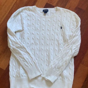 Vit kabelstickad tröja Polo Ralph Lauren -  ÄKTA EN HELT NY Snygg vit kabelstickad tröja från Polo Ralph Lauren. Det är nog den ändå äkta Ralph lauren tröjan på plick. med klassisk rund hals och broderad marinblå logga på bröstet. Tröjan har långa ärmar och ribbade muddar vid ärmslut och nederkant. Den är helt ny inga defekter. Storlek L(14 16) passar folk som har xs. Nytt pris 2195 mitt pris 1100 😊😊❤️❤️ÄKTA