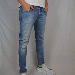 Dondup George - Riktigt feta mörkblåa Dondup jeans i modellen George med slitningar. Jeansen är i storlek 34 och är i väldigt gott skick, dvs har inga tecken på användning.                                         Innerbenslängd: 72cm.  Midjemått: 40cm         Vid frågor eller funderingar är det bara att höra av sig, och kom ihåg, alltid 14 dagars ångerrätt hos oss på Revalo!