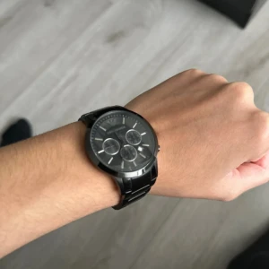 Svart Emporio Armani klocka - Använt lite, den har bara suttit så jag tänker sälja den. Batteri måste kanske bytas. Snygg svart klocka från Emporio Armani med metallarmband och rund urtavla. Urtavlan har tre mindre visartavlor, datumvisning och silvriga detaljer. 