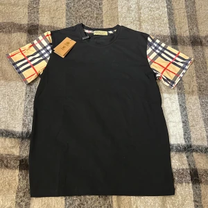 Burberry T-shirt  - Säljer en svart T-shirt från Burberry med rutiga ärmar, tröjan är helt ny och Storlek M, lapparna hänger kvar och medföljer vid köp. Vid frågor eller intresse är det bara att skriva ✍️ Priset kan diskuteras inom snabbaffär eller bundleköp Mvh ✅