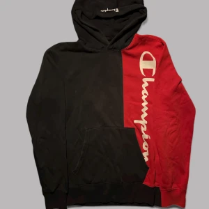 Champion hoodie svart/röd S - Snygg hoodie från Champion i storlek S med delad design i svart och rött. Stor vit Champion-logga längs ena sidan, huva och magficka. Mjuk insida i fleece och långa ärmar. Perfekt för dig som gillar streetwear och sportig stil. Snörena är bort tappade.