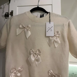 Vit stickad tröja med rosetter från JS - Supersöt vit stickad tröja från JS med korta ärmar och flera stora satinrosetter framtill och på ärmarna. Tröjan har rund hals och en mjuk, fluffig känsla som gör den extra mysig. Perfekt för dig som gillar gulliga detaljer och vill sticka ut.    Står ingen storlek men är nästan säker på att det är XS/S💕 Den är även helt ny!! Ordinarie pris 699kr men säljer för 480kr, pris går att diskutera vid snabb affär! Så kom gärna med prisförslag🥰