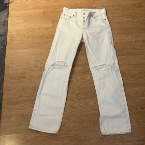 Vita raka jeans från Junkyard, strl 27 - Snygga vita jeans från Junkyard i rak modell med slitna detaljer vid knäna. Klassisk femficksdesign, knappar i silver och kontrastsömmar. Perfekt för dig som gillar en clean och avslappnad look.