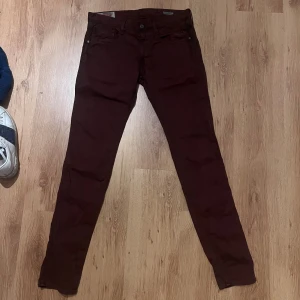 Replay Anbass vinröda slim jeans 32/34 - Snygga vinröda Replay Anbass jeans i slim fit med klassisk femficksdesign och detaljerade sömmar. Byxorna har normal midja och raka ben, tillverkade i mjuk bomull med lite stretch för extra komfort. Jeansen har konstiga fläckar Perfekt för dig som gillar stilrena och moderna jeans. Midja 40cm längd 105cm (77)