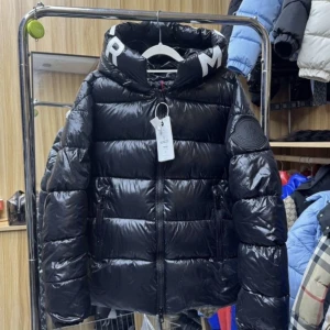 Svart pufferjacka från Moncler - Säljer en svart pufferjacka från Moncler med glansig finish och stor huva med vita bokstäver. Jackan har dragkedja framtill, två sidofickor med dragkedja och Moncler-logga på ärmen. Perfekt för kalla dagar och riktigt snygg streetstil.