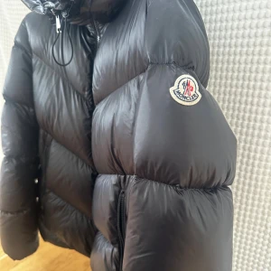 Svart Moncler pufferjacka med huva - Jättefin Monclerjacka köpt för 14 000kr från NK i Göteborg. Modellen ”CHAMBON GIUBBOTTO CHAMBON SHORT PARKA” storlek 2. Pris kan diskuteras