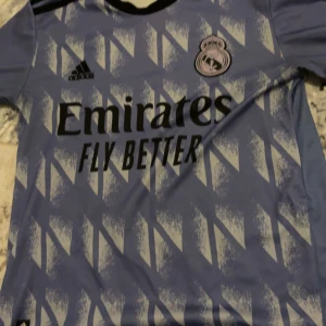 OG Real Madrid bortatröja Adidas nr 9 benzema - Snygg Real Madrid bortatröja från Adidas i ljusblått med vita och mörkblå detaljer. Tröjan har korta ärmar, tryckt klubbmärke, sponsorlogga och nummer benzema 9 på ryggen. Tillverkad i lätt och ventilerande material, perfekt för fotboll eller att bära till vardags.