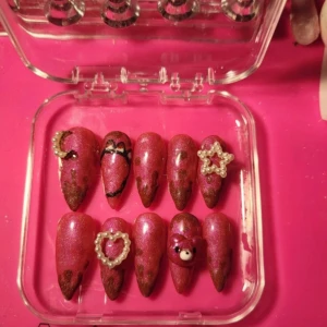 Rosa glittriga lösnaglar med dekorationer - Säljer ett set med tio spetsiga lösnaglar i skimrande rosa med bruna detaljer. Naglarna har dekorationer som pärlhjärtan, pärlstjärna och en söt 3D-nalle. Perfekt för dig som vill ha extra cute och unik nagelstil. Kommer i genomskinlig ask.