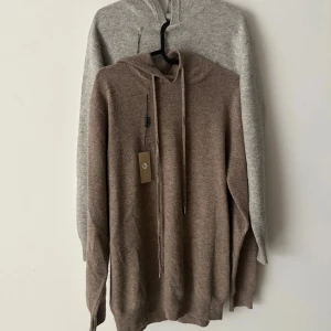 Kashmirhoodie i beige och grå - Två helt nya hoodies i 100% kashmir, en i beige och en i ljusgrå. Båda har huva, snörning och långa ärmar. Mjuka och lyxiga med ribbade muddar vid ärmslut och nederkant. Perfekt för dig som vill ha en chill och stilren look. 