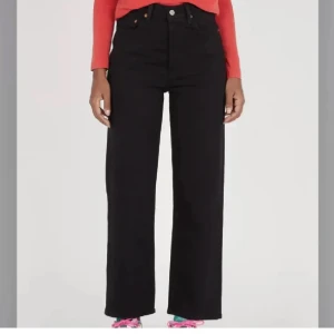 Svarta Levi's ribcage - Svarta jeans från Levi's modell 501 med hög midja och raka, breda ben. Klassisk femficksdesign och knappgylf. Jeansen är tillverkade i slitstarkt denim och har en snygg läderpatch baktill i midjan.