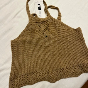 Beige stickad linnetopp från FB Sister - Säljer en beige stickad linnetopp från FB Sister med smala axelband och snygga virkade detaljer upptill och längs nederkanten. Toppen har en lätt croppad passform och är perfekt för varma dagar. Materialet är mjukt och luftigt, vilket gör den superbekväm.
