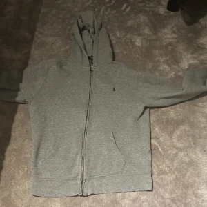 Grå hoodie från Polo Ralph Lauren S - Säljer en grå hoodie från Polo Ralph Lauren i storlek Small. Tröjan har huva, hel dragkedja framtill och två fickor. Klassisk liten Polo-logga broderad på bröstet. Perfekt för chill dagar och enkel att matcha med jeans eller joggers.